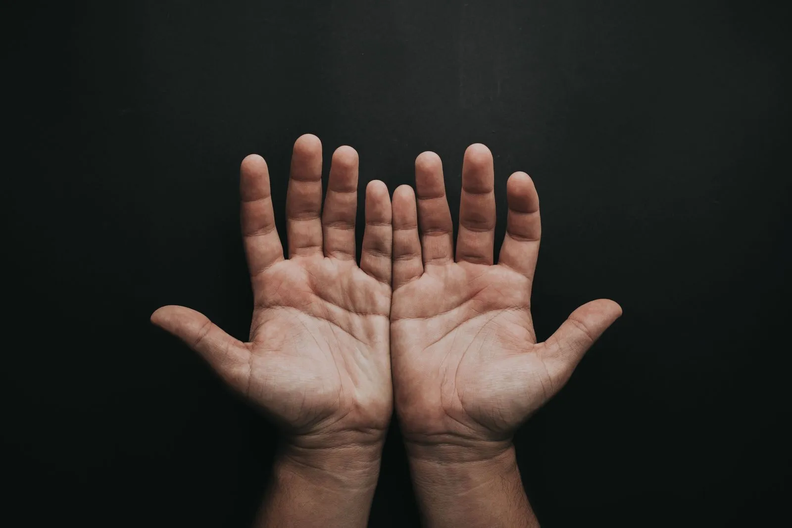 Zwei geöffnete Handflächen vor dunklem Hintergrund, Finger und Hautfalten gut sichtbar
