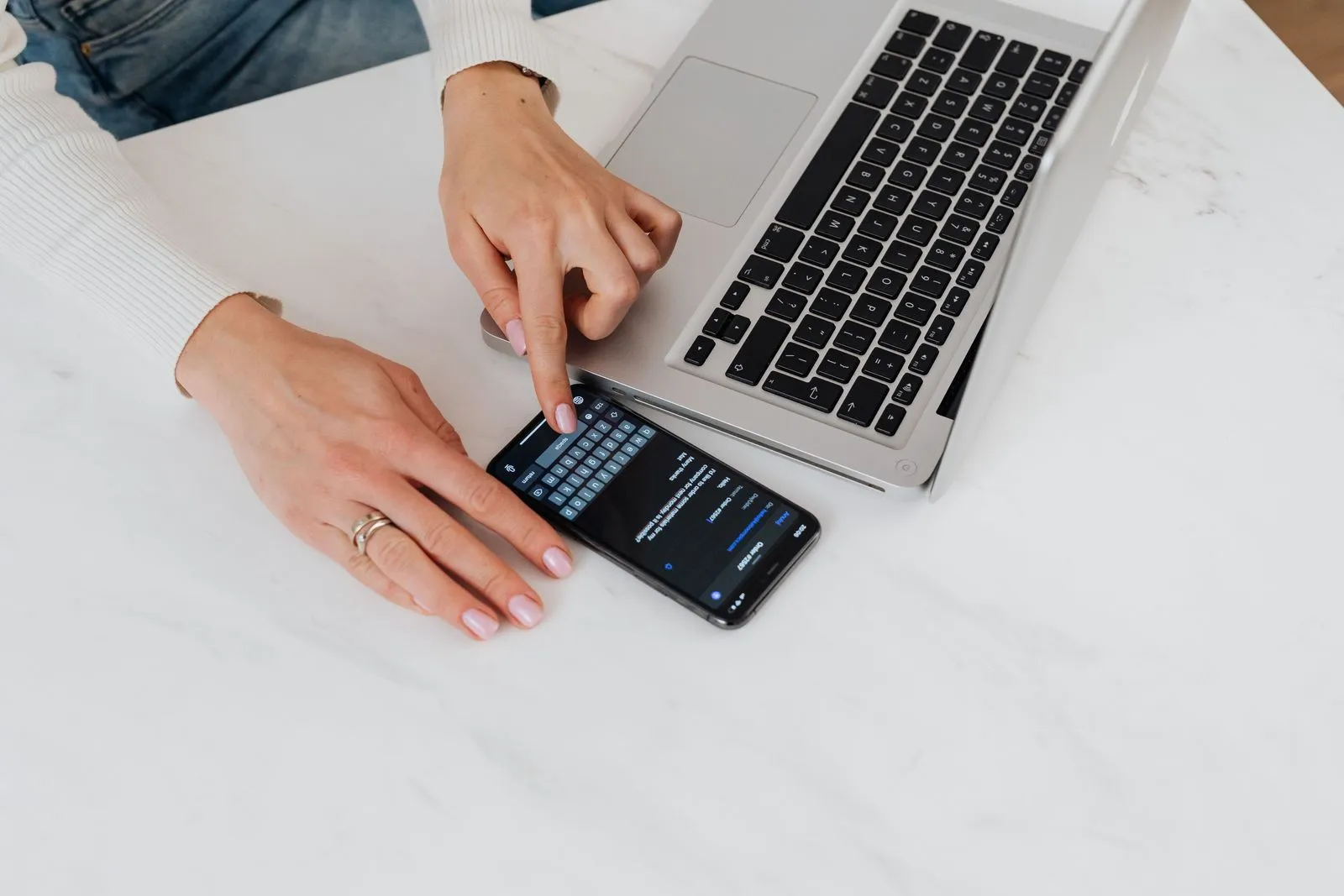 Hände an einem Smartphone und einem Laptop auf einem hellen Tisch