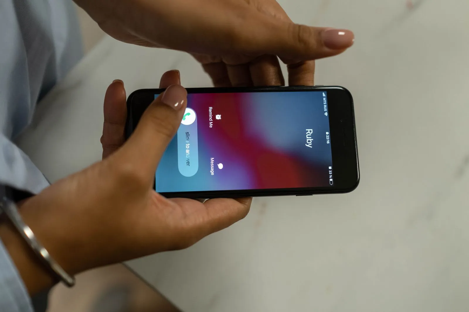 Hände halten ein Smartphone, auf dem ein eingehender Anruf mit einem Namen angezeigt wird