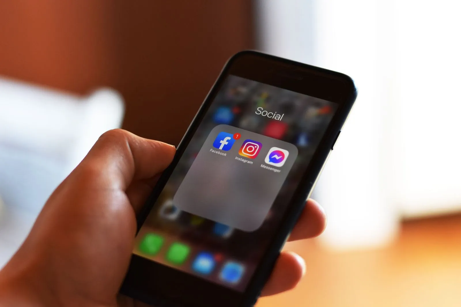 Eine Hand hält ein Smartphone mit einem Ordner, in dem die Apps Facebook, Instagram und Messenger liegen