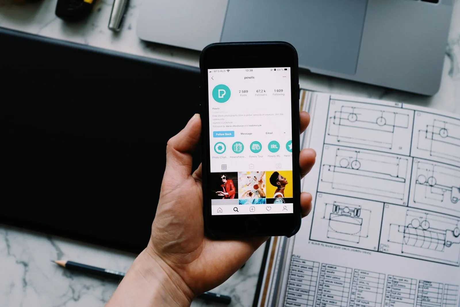 Eine Hand hält ein Smartphone mit einem geöffneten Social-Media-Profil über einem Schreibtisch