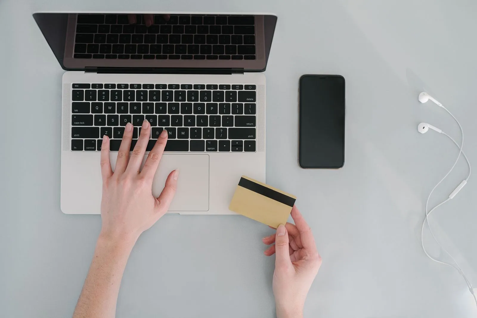 Hände an einem Laptop, eine Hand hält eine goldene Bankkarte, daneben liegt ein Smartphone