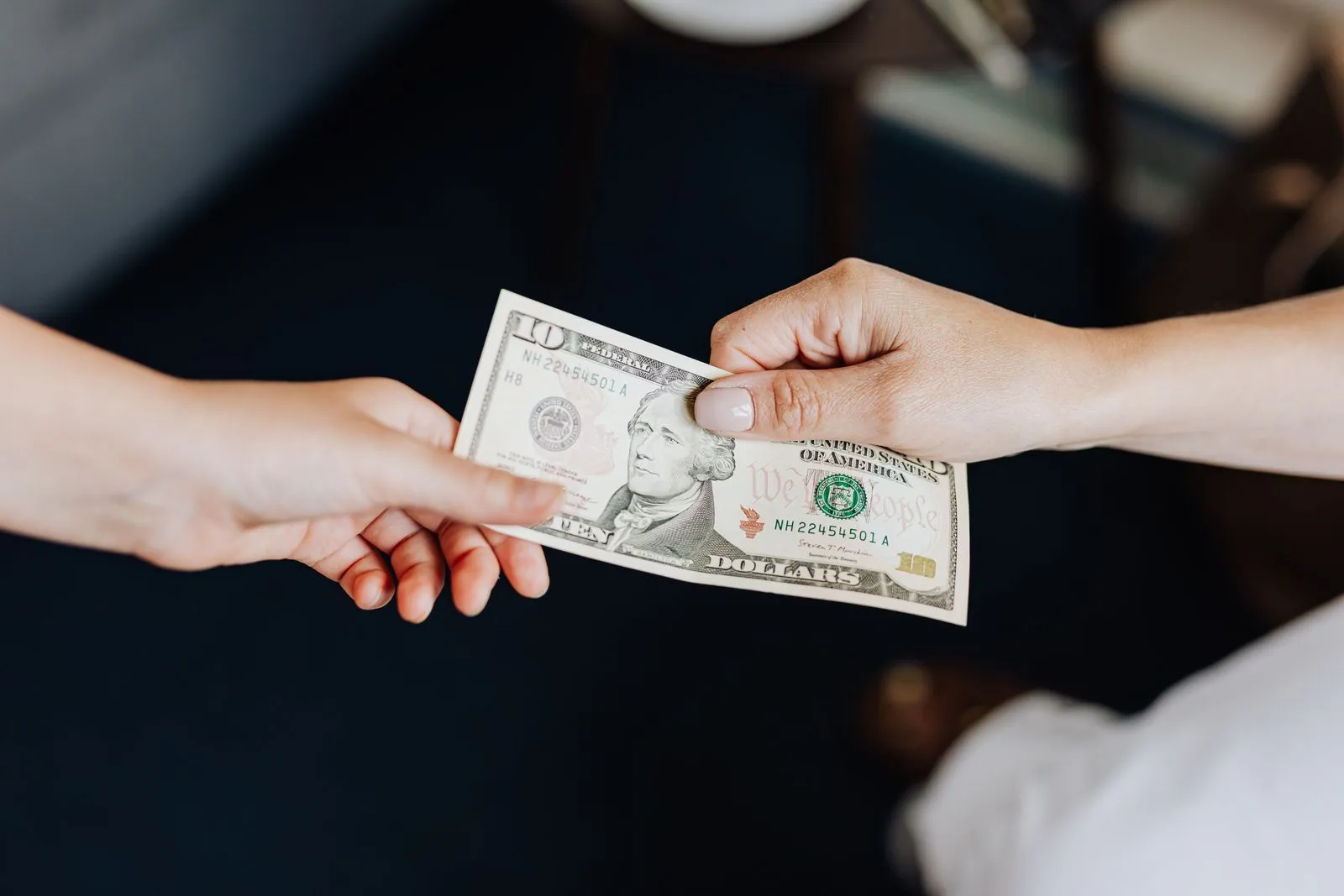 Two hands passing a ten-dollar bill across a table