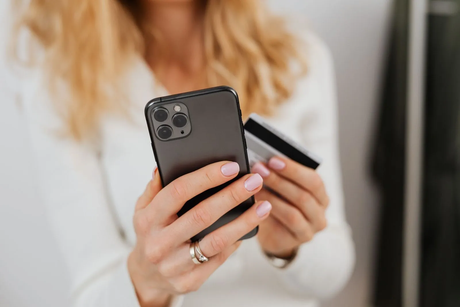 Hands holding a smartphone and a bank card in front of a light background