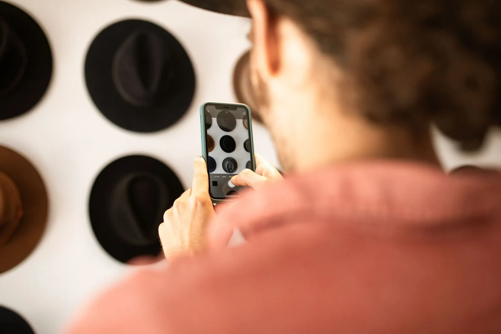 Person fotografiert mit dem Smartphone Hüte an einer Wand