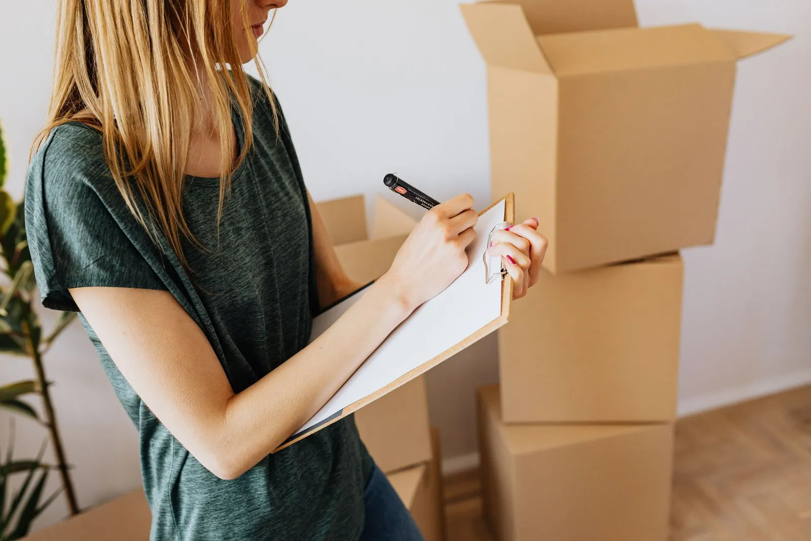 A woman writes on a clipboard in front of stacked moving boxes