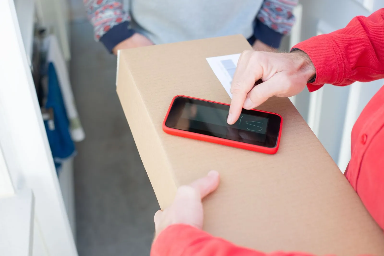 Hände tippen auf einem Smartphone, das auf einem Paketkarton an einer Haustür liegt