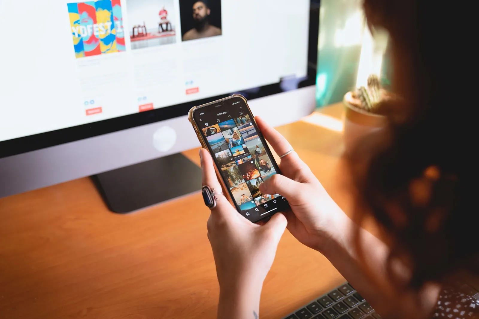 Hände halten ein Smartphone mit einem Raster aus Profilfotos vor einem Computerbildschirm
