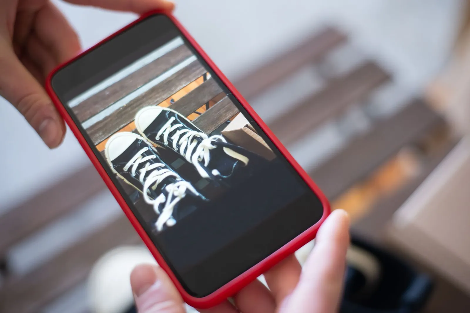 Hände fotografieren ein Paar schwarze Sneaker mit dem Smartphone