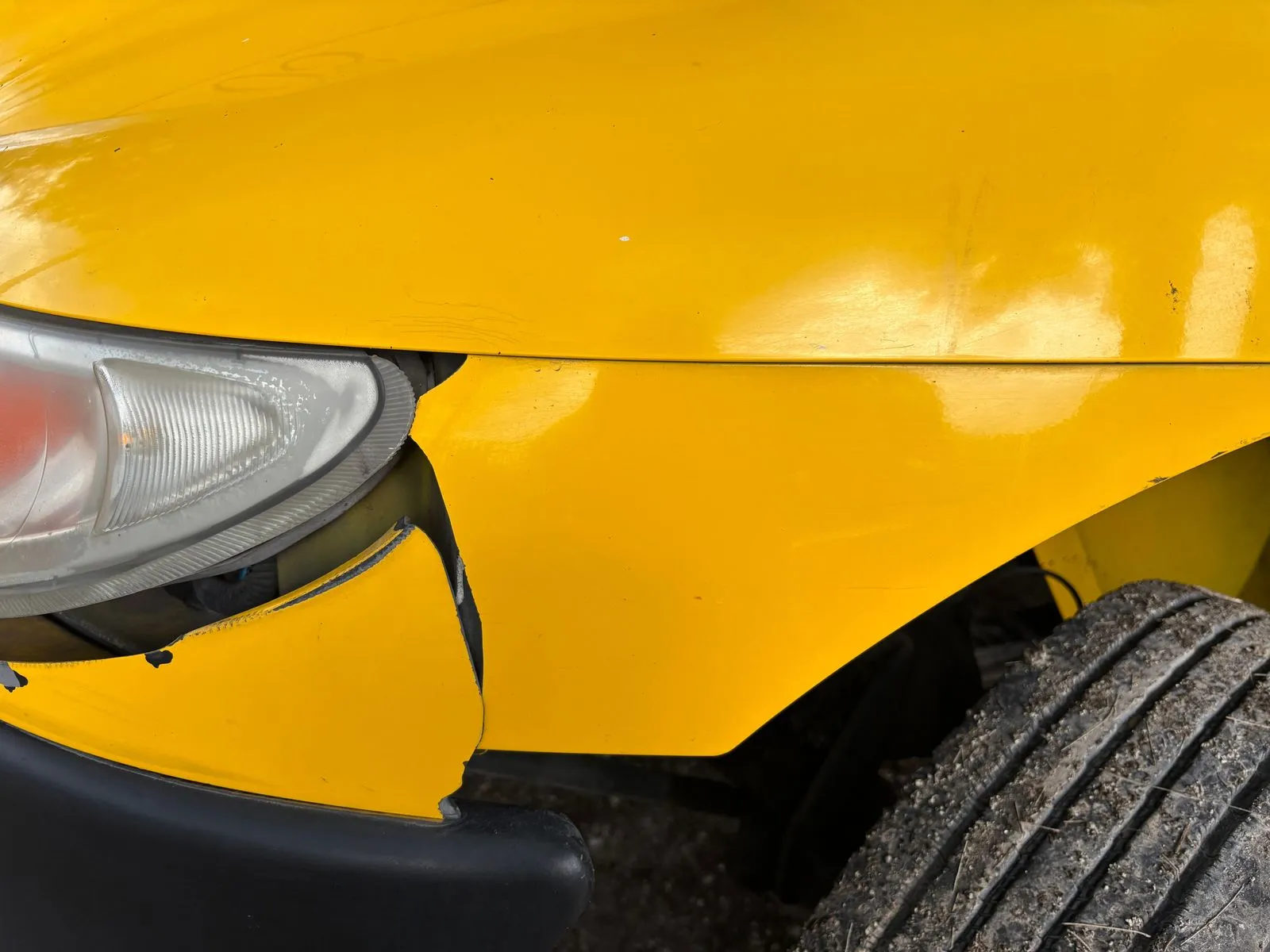 Cracked yellow body panel below a headlight, with a tire in the corner