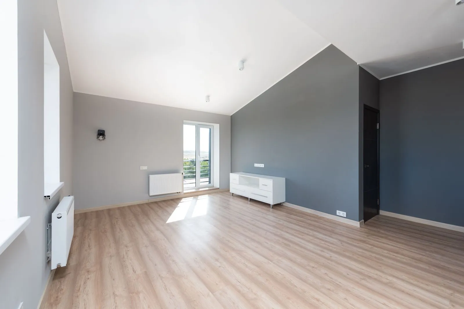 Fast leere, helle Wohnung mit Dachschräge, Holzboden, grauen Wänden und einer Balkontür