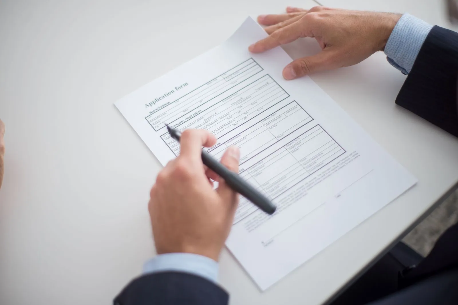 Hands with a pen over a printed application form on a white desk