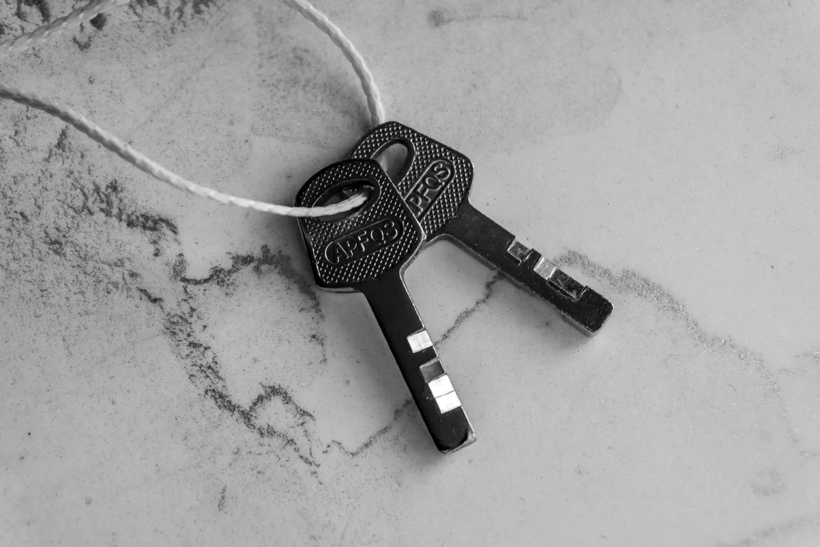 Two keys on a string lying on a light marble surface
