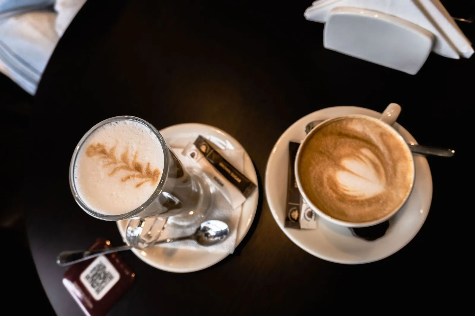 Two cups of coffee with latte art on a dark café table, photographed from above