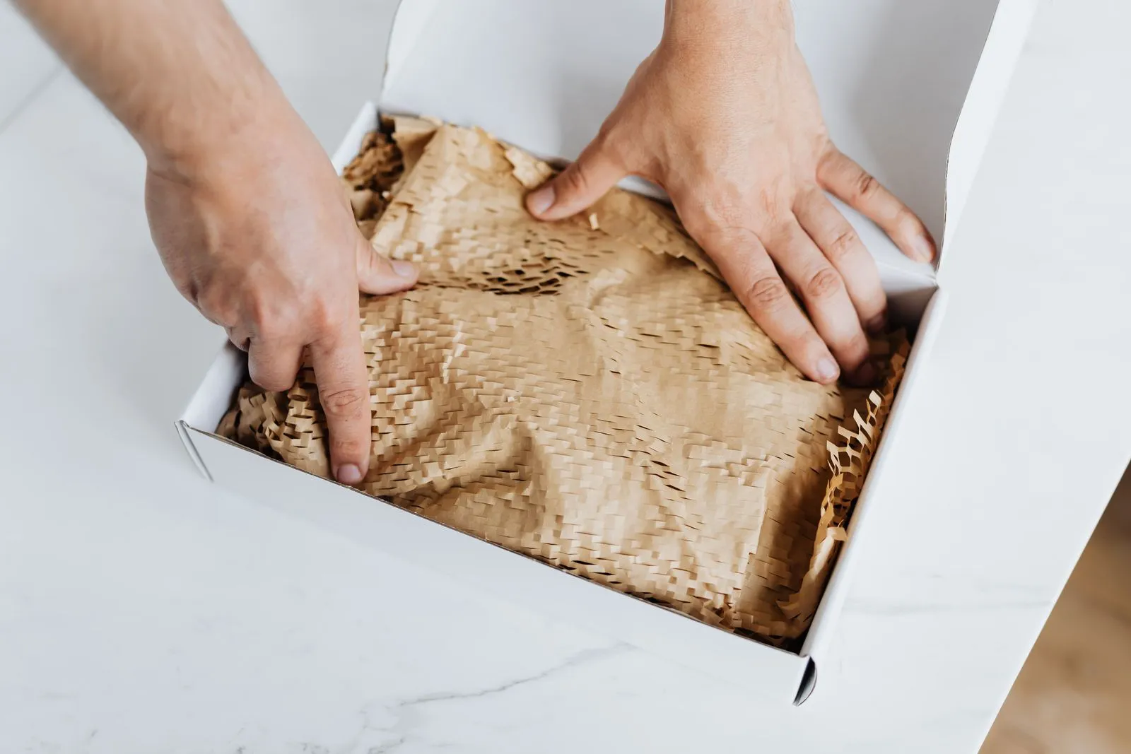 Zwei Hände legen Papierpolster in einen weißen Versandkarton