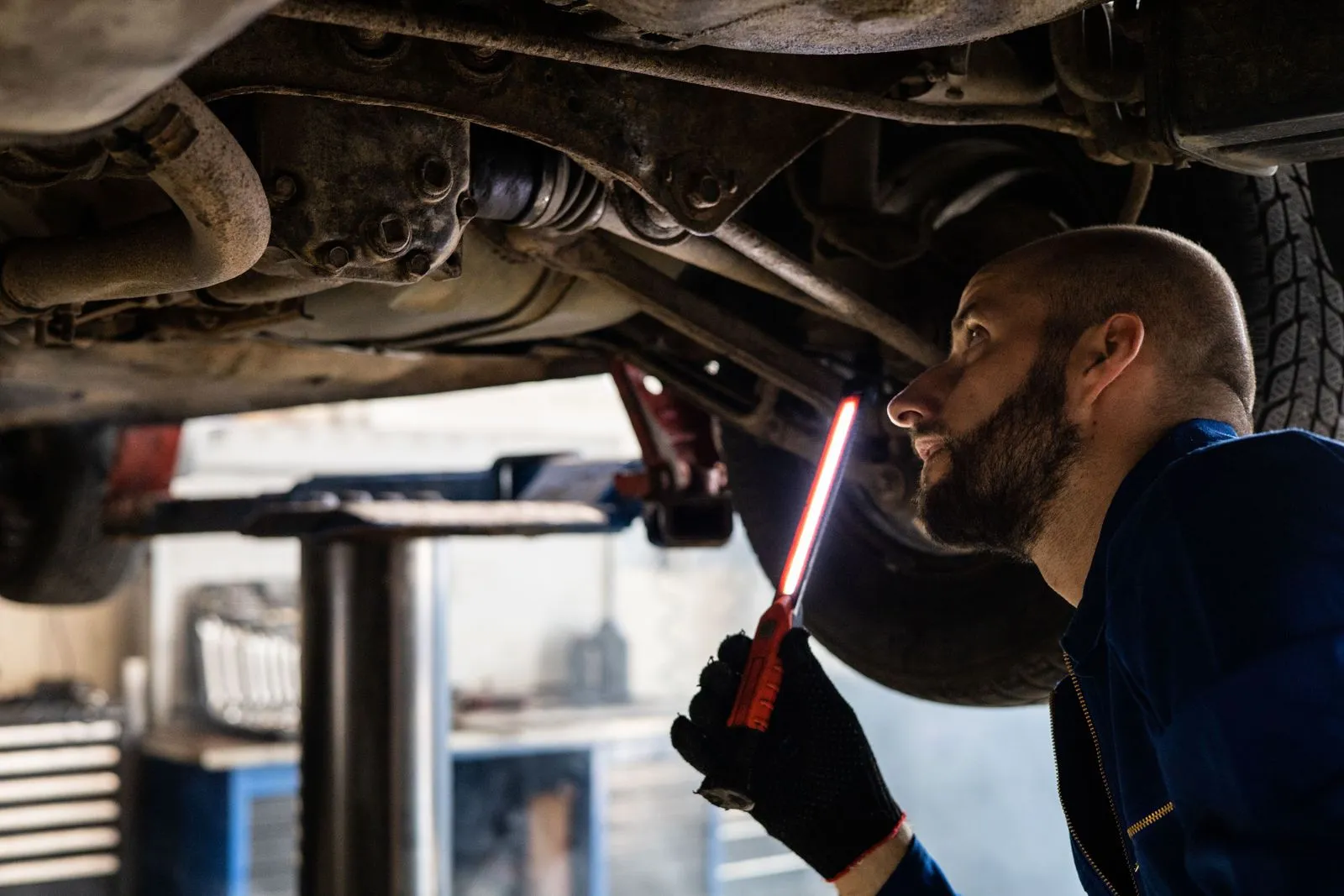 Un meccanico controlla con una lampada da lavoro il sottoscocca di un'auto sollevata in officina