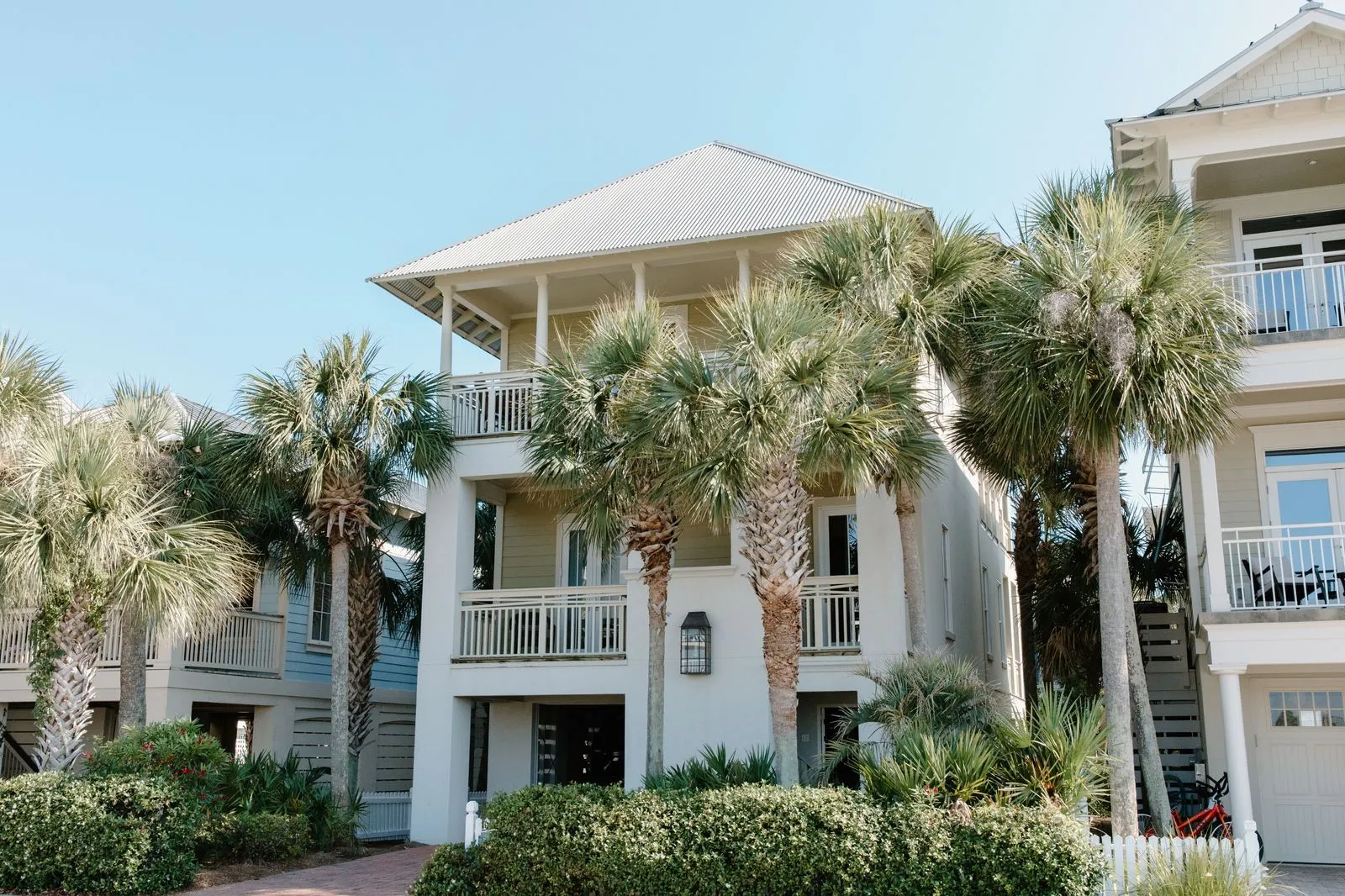 Beach house with white balconies behind palm trees under a clear blue sky